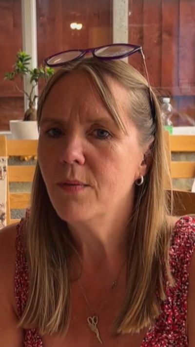 Mia Hansson looking straight at the camera. She wears a pink floral patterned top. She has glasses propped on her forehead.