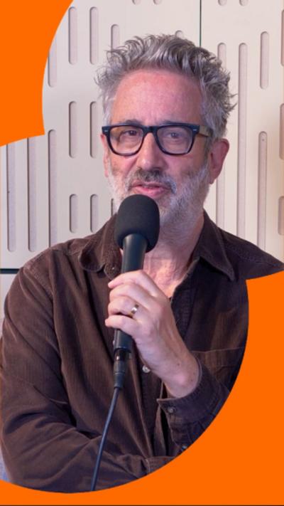 A man with short grey hair and glasses speaks into a microphone