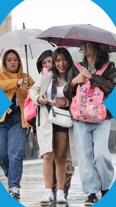 Women shelter under umbrellas during rainfall while walking across Westminster Bridge in London