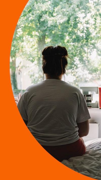 A woman sits with her back to camera looking out the window at some trees