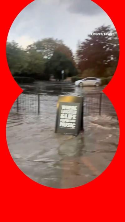 A pub sign in front of a fence surrounded by flood water.