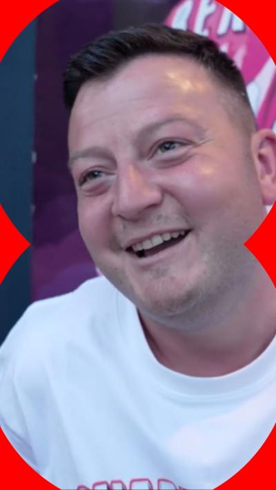 A man with dark brown hair smiling, wearing a white t-shirt