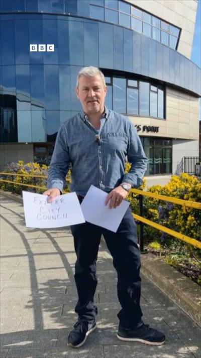 Miles Davis stands in front of a leisure centre holding a piece of paper that says Exeter City Council.