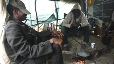 migrants sit around cooking pot