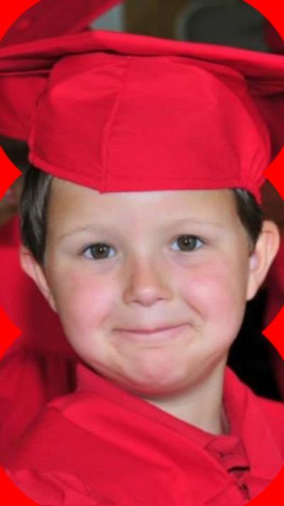 Jordan Smelski has brown eyes and brown hair. He is wearing a red mortarboard and gown from a school graduation ceremony.