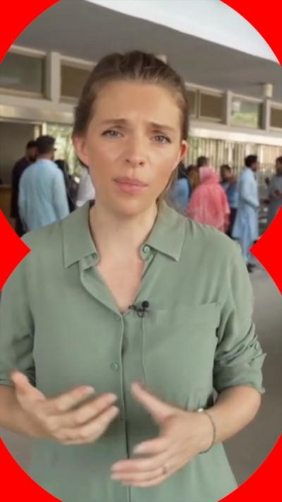A woman in a green shirt stands in front of a hospital.