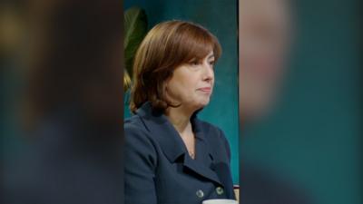 Lucy Powell sits in a blue suit, looking to the right. She has shoulder length brown hair