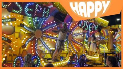 A carnival float lit up and the Happy News logo