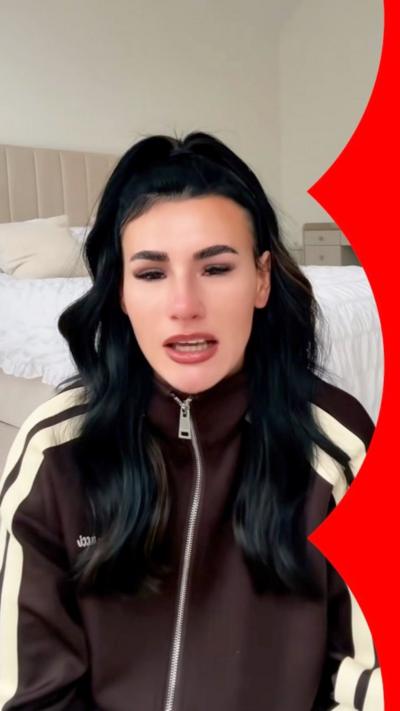 A woman, Brittany Miller, with dark hair and a brown sports jacket, looking tearful to camera. A still from a video.