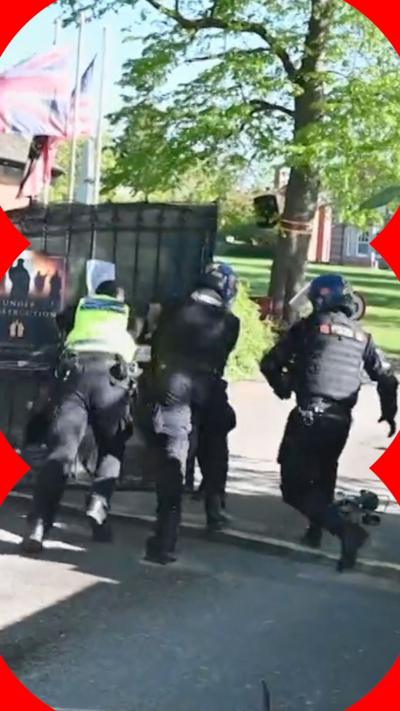 Three police officers push a gate