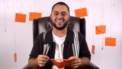 A person sits at a chair opening an orange envelope