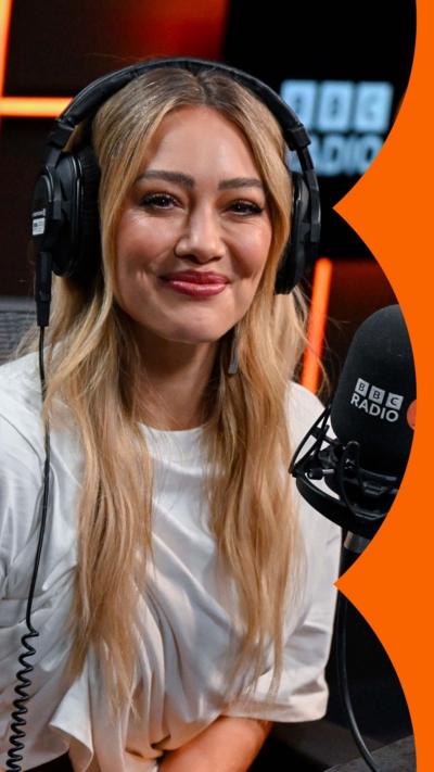 Hilary Duff in the Radio 2 studio. She has blonde hair and wears a white T-shirt