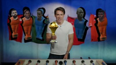 In an edited image, a man in white t-shirt stands behind a foosball table with the Afcon trophy stuck over his extended right hand. Foosball players with real players' heads are cut out and displayed behind him