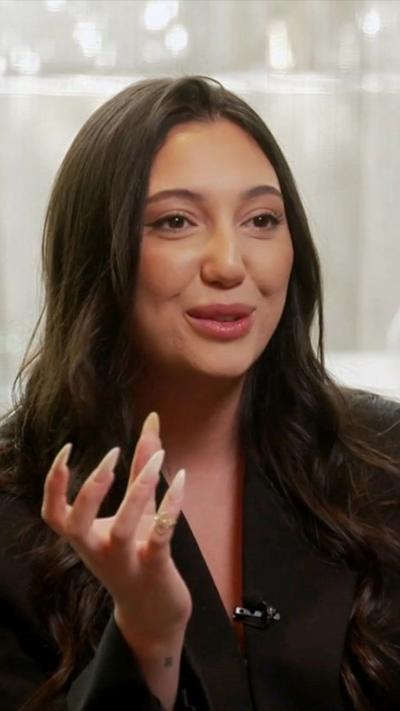 Yuval Raphael speaks during an interview - she has long brown hair and wears a black jacket