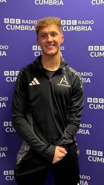 Thomas Atkinson standing in front of a purple BBC Cumbria board
