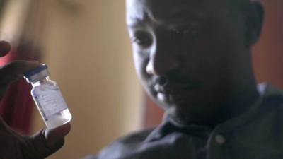 Alan Kasujja holding a bottle of medicine