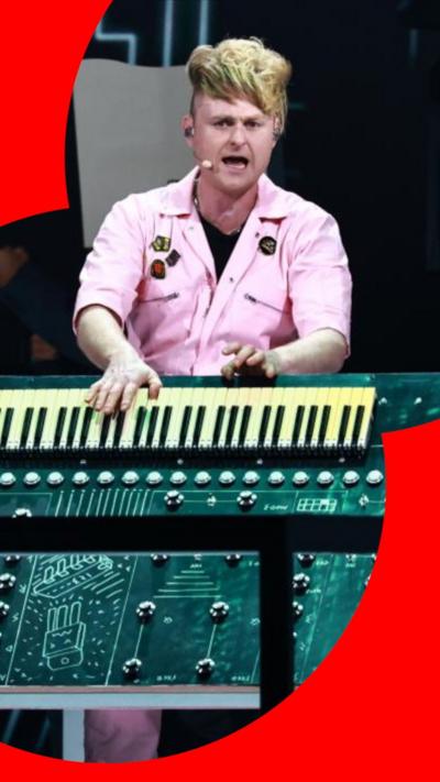Look Mum No Computer performing behind a piano, wearing a pink jumpsuit