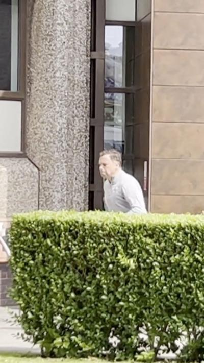 Ken Skates running in front of a business, he is stood behind a bush