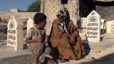 Aisha Ali and Ahmed Mohammed Bitar sit in the cemetery.