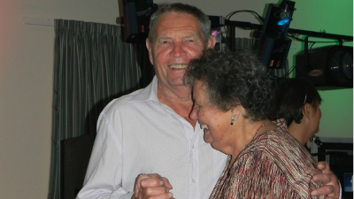 Bob and Sylvia dance together at a function. Bob is wearing a white shirt and Sylvia is wearing a multi-coloured top.