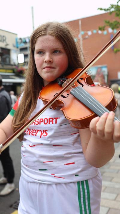 A girl in a white sports top playing a fiddle. 