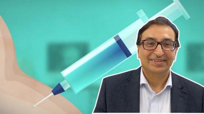 Dr Salim Modan in front of a vaccine graphic