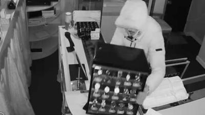 Burglar picks up a display case of watches while robbing a jeweller's.