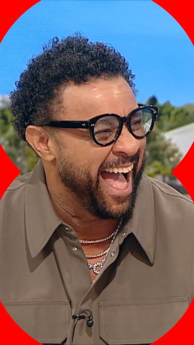 Shaggy laughs in the BBC Breakfast studio. He wears a brown shirt and black glasses