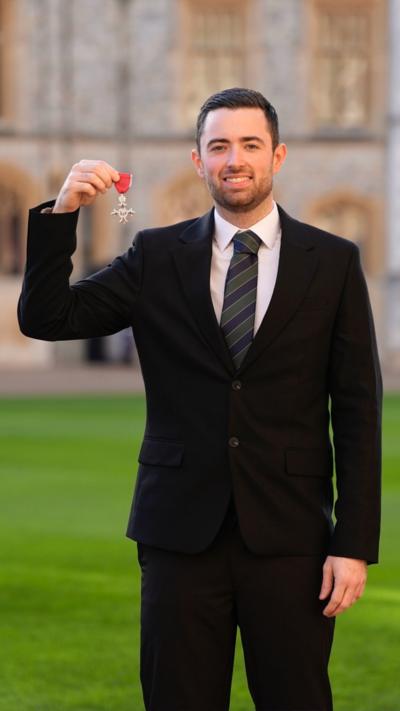 Luke Humphries holds up his MBE medal.