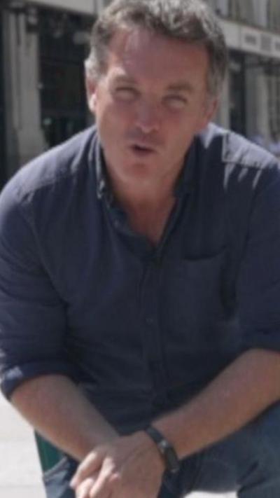 A man with short hair crouches on the floor