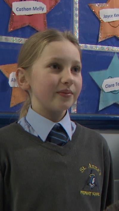 A young girl in a grey school jumper, with a blue shirt and tie underneath. 