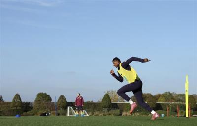A man, Marcus Rashford, wears a black tracksuit with a yellow high vis vest and football boots. He is running.