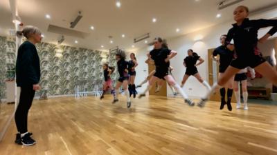 Sharon, tidsear nan dannsairean, air beulaibh a' chlas agus na nigheanan a' dannsa. 