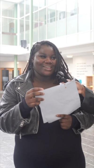 Girl wearing a leather jacket smiles and holds her results paper