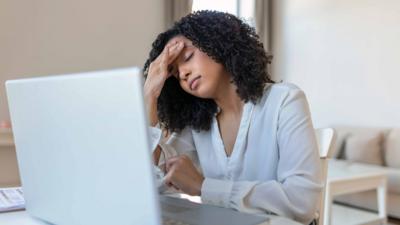 Woman sits in front of laptop holding her head