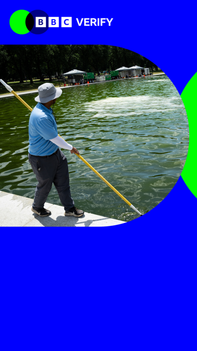 A man wearing a blue t-shirt and a white hat holds a pole with a net as he sweeps it throuh the water of the reflecting pool