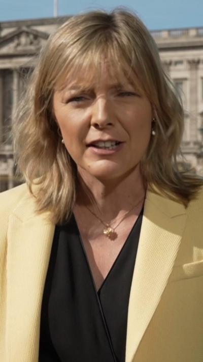 Ellie Price, with blonde hair and a yellow jacket, stands in front of Buckingham Palace.