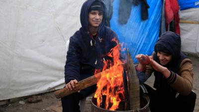 Two migrants from Kuwait try to warm up in a camp for migrants called the "jungle", in Calais, northern France, February 25, 2016.