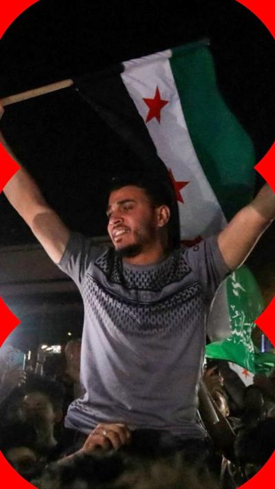 Man holding with hands raised above his head holding Syrian flag in one hand
