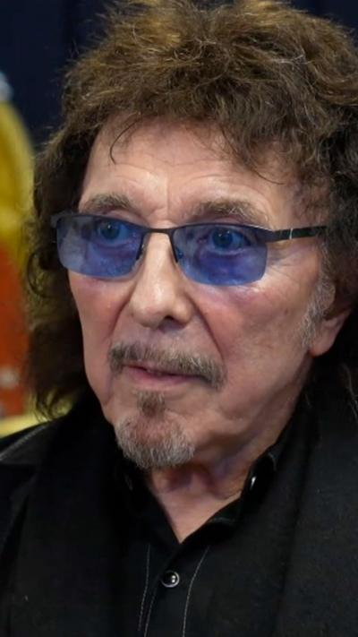 A man with blue-tinted glasses, beard and dark hair in a black jacket with black shirt.