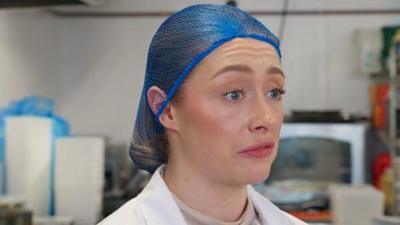 A stressed looking woman wearing a blue hairnet in a kitchen