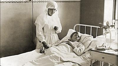 Black and white image of a patient in a hospital bed with a medical professional taking their pulse