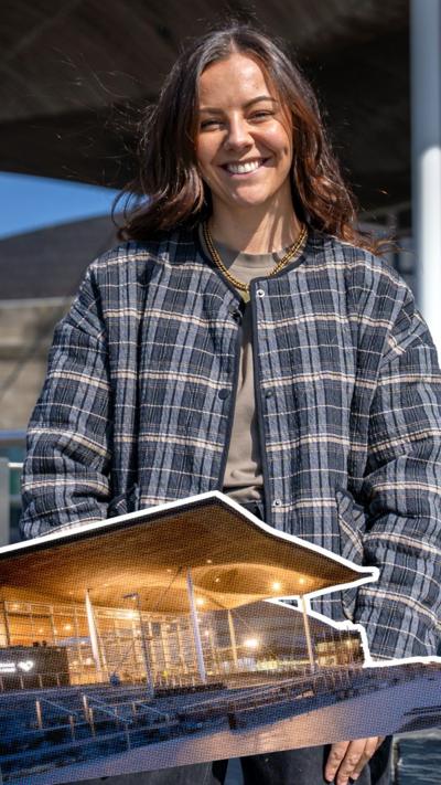 girl smiling outside the Senedd building, wearing a plaid blue jacket.
