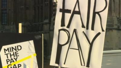 Protest placards reading 'Mind the Pay Gap' and 'Fair pay'