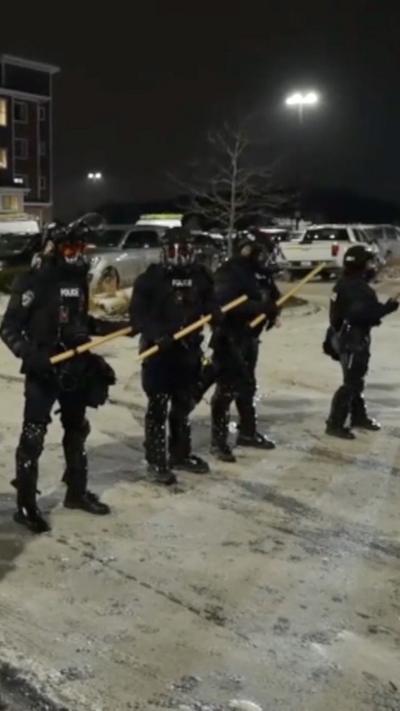 Law enforcement officers stand in a parking lot with riot gear on