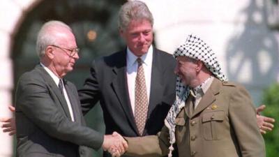 US President Bill Clinton standing between PLO leader Yasser Arafat as he shakes hands with Israeli Prime Minister Yitzhak Rabin