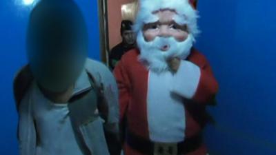 A policeman dressed as Santa holding a man under arrest - December 2016