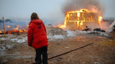 A person looks on at a blazing structure