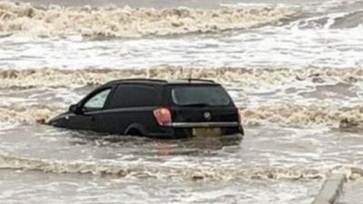 Car submerged in waves on beach