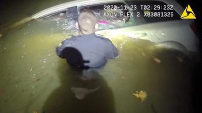 Police officer in water in front of sinking car